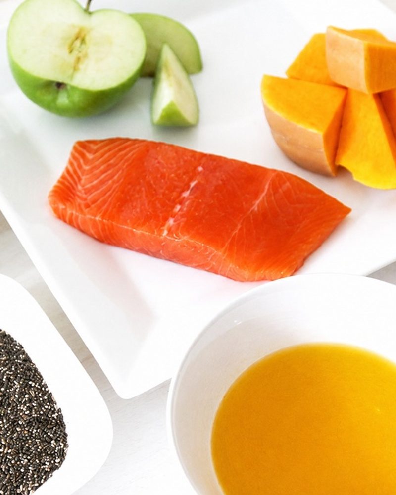 Raw salmon, green apple, squash, oats, chia seeds, broth, and yogurt arranged in white dishes.