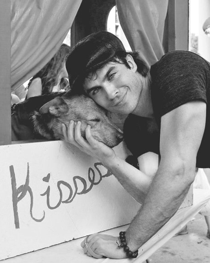 Black and white lifestyle photography of Ian Somerhalder cuddling a dog at a kissing booth.