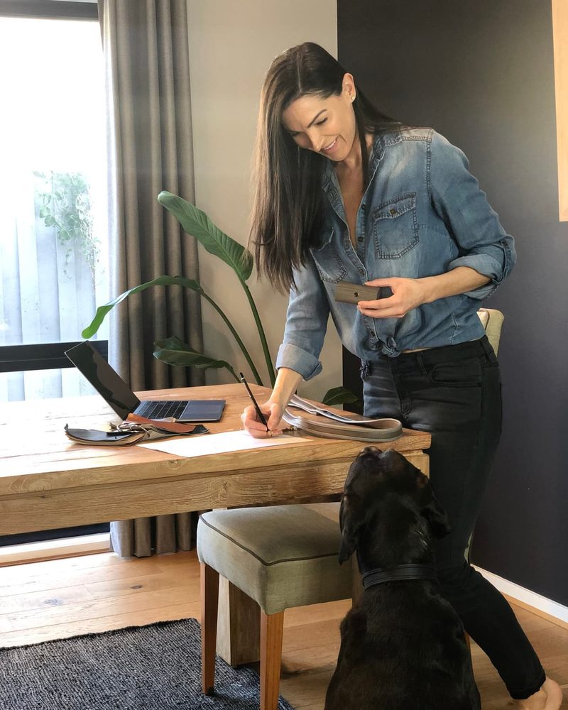 Molly Barker designing luxury pet accessories at her desk with leather samples and her black dog.