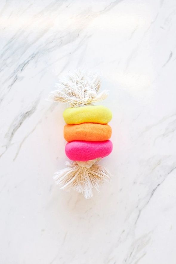 Three colourful fabric rings threaded onto a frayed white rope, forming a dog toy on marble.