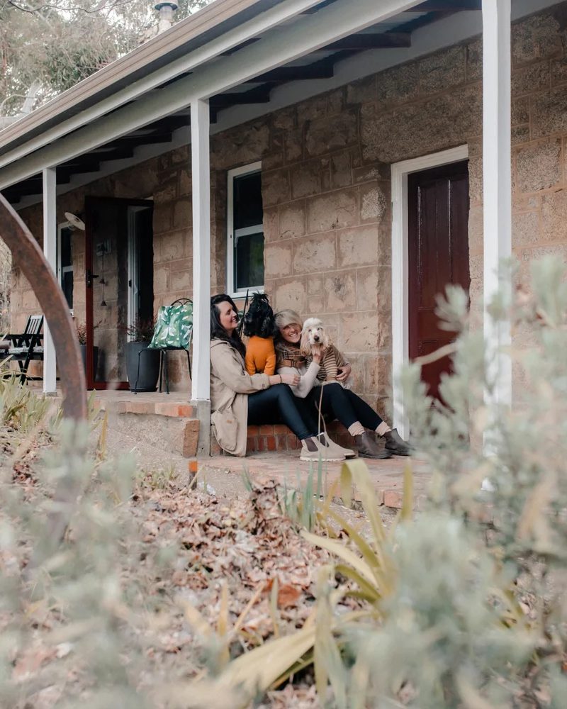 Two people with dogs sitting on the stone porch of Granite Cottage, pet-friendly accommodation in Beechworth.