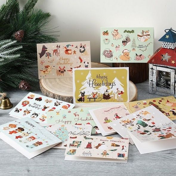 Assorted Christmas cards featuring illustrated dogs and other pets arranged beside festive greenery and a lantern.