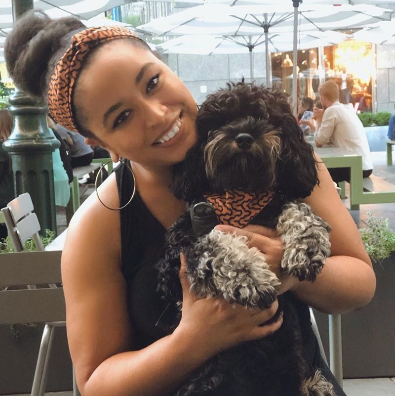 Smiling Black woman holding a small dog in matching patterned accessories from a Black-owned pet brand.