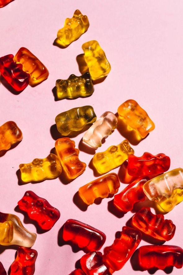 Assorted translucent gummy bears in red, orange, yellow, and white scattered across a pink background.