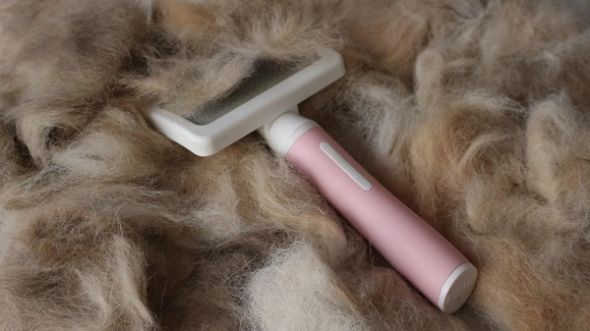 A pink and white pet grooming brush sits on a large pile of shed dog hair.