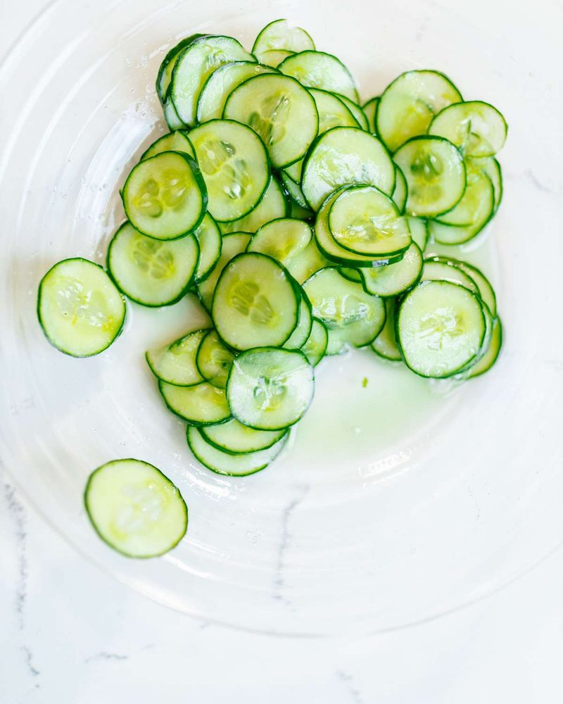 Thinly sliced fresh cucumbers in a clear glass bowl on a white countertop.